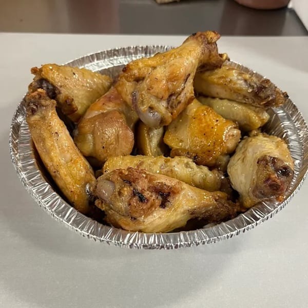 A foil container filled with golden-brown, crispy chicken wings from Big T's Pizza.