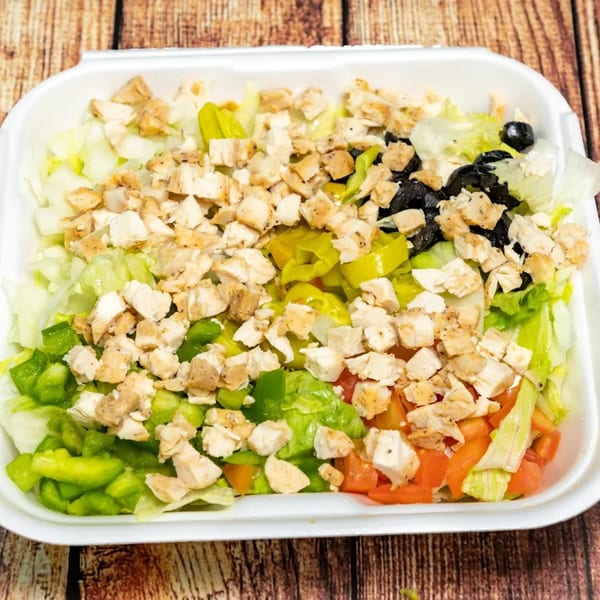 Chicken salad with lettuce, green peppers, tomatoes, black olives, and banana peppers in a white container.