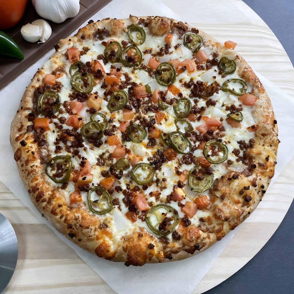 Big T's Pizza with ground meat, jalapeños, tomatoes, and onions on a wooden peel.