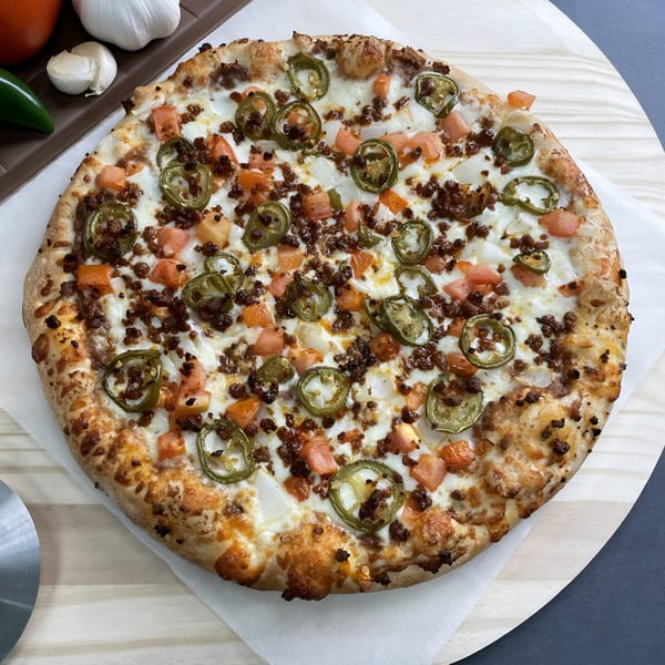 Big T's Pizza with ground beef, jalapenos, diced tomatoes, and onions on a wooden peel.