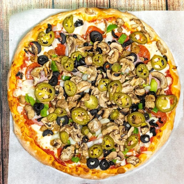 Big T's Pizza with pepperoni, mushrooms, black olives, jalapeños, and onions on a wooden table.