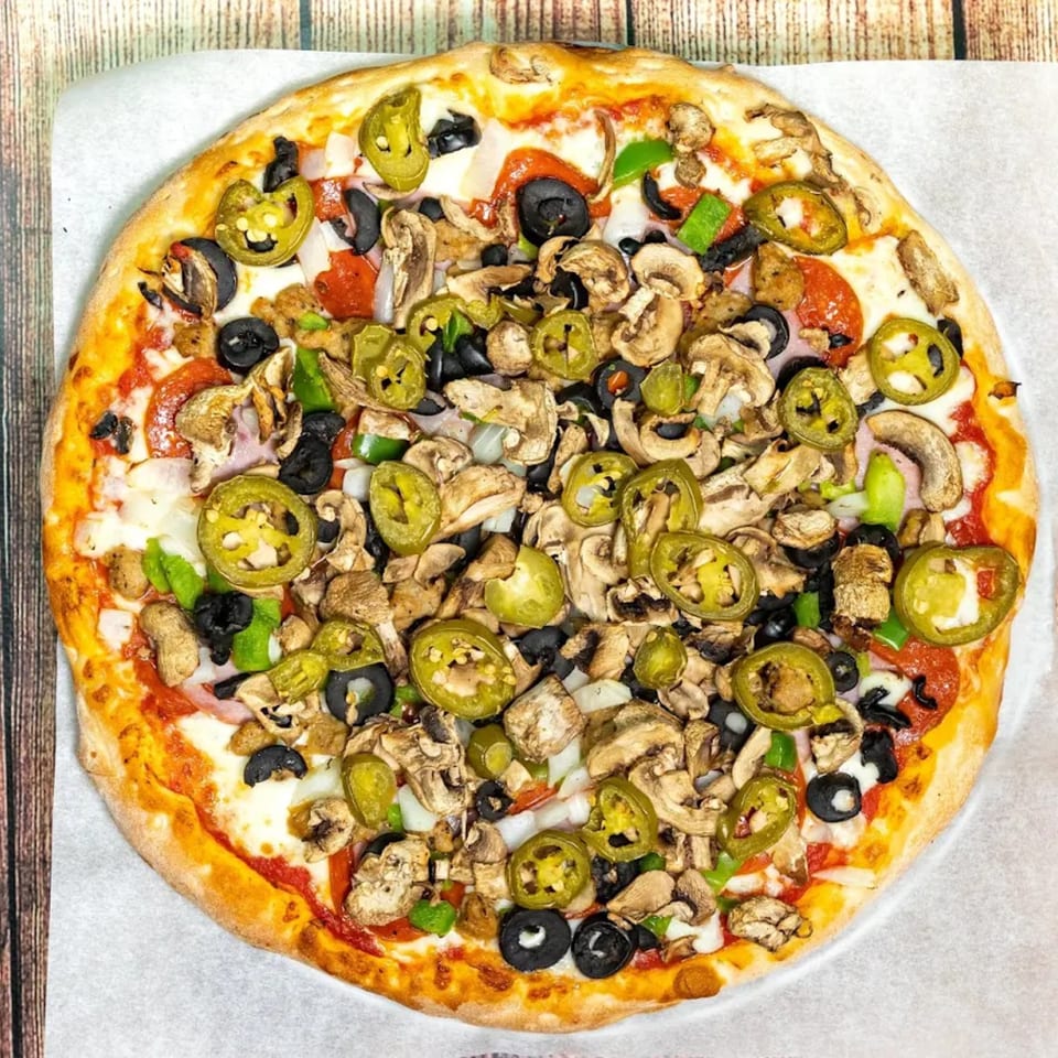 Big T's Pizza with pepperoni, mushrooms, black olives, jalapeños, and onions on a wooden table.