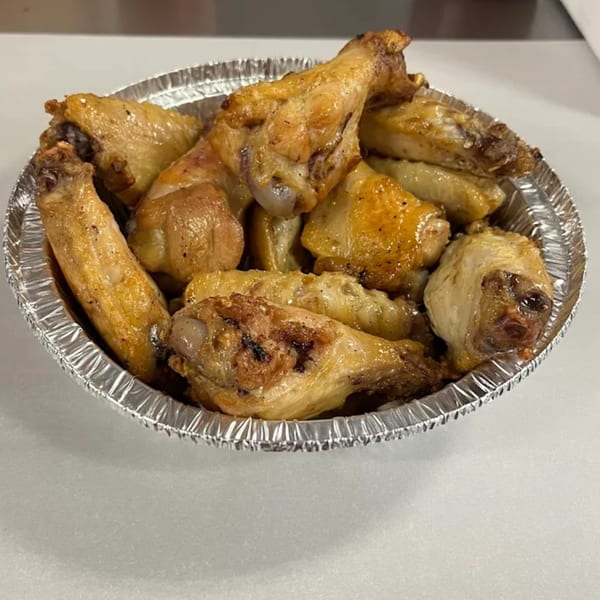 A foil container filled with golden-brown, crispy chicken wings from Big T's Pizza.