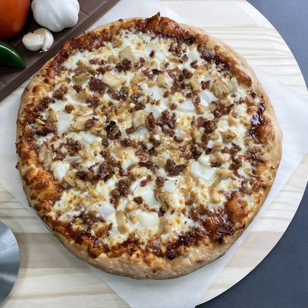 Big T's Pizza with chicken, onions, and bacon on a wooden peel with fresh ingredients.