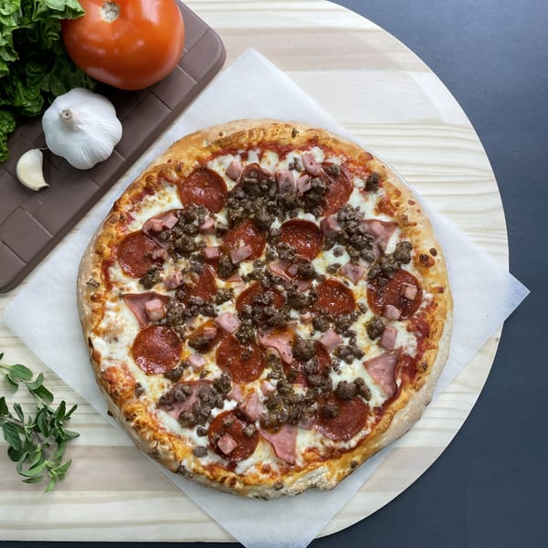 Big T's Pizza with pepperoni, ham, and ground beef, alongside fresh garlic, tomato, and greens.