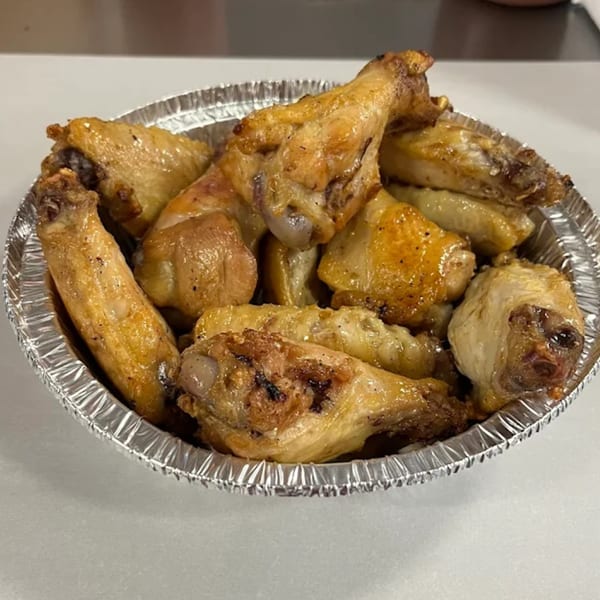 A foil container filled with golden-brown, crispy chicken wings from Big T's Pizza.