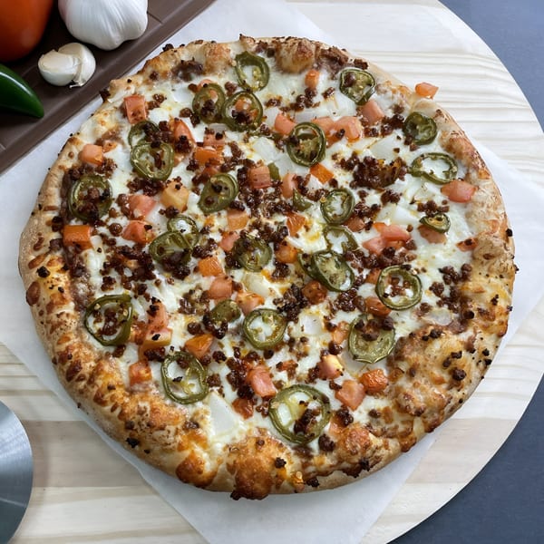 Big T's Pizza with ground beef, jalapeños, tomatoes, and onions on a wooden peel.