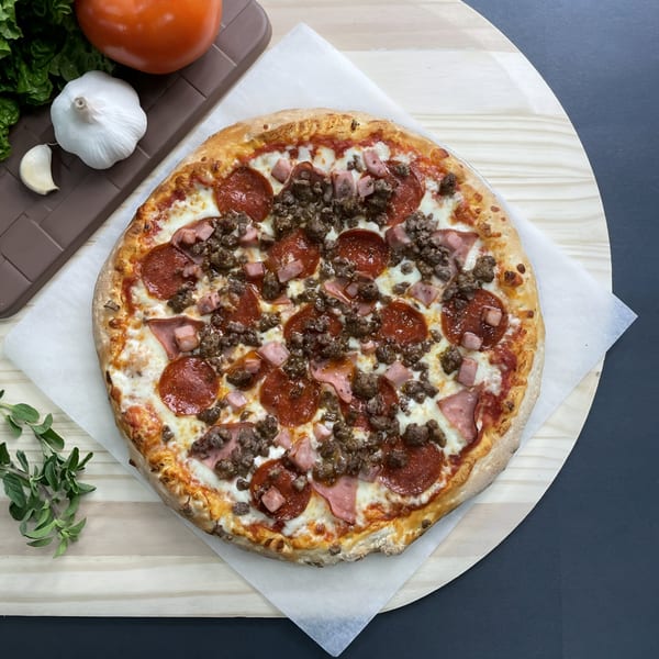 Big T's Pizza meat lover's pizza with pepperoni, ham, and ground beef, on a wooden peel.