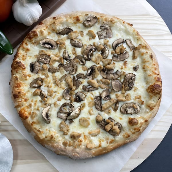 Big T's Pizza white pizza with mushrooms and chicken, on a wooden peel.