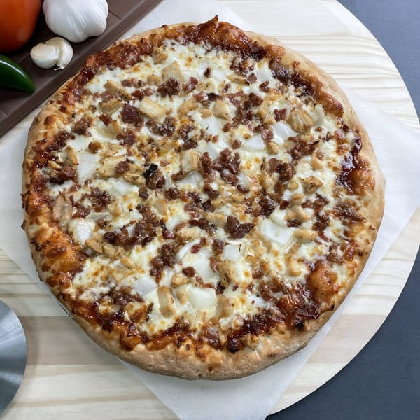Big T's Pizza with chicken, bacon, and onions on a wooden peel, with garlic and jalapeños.