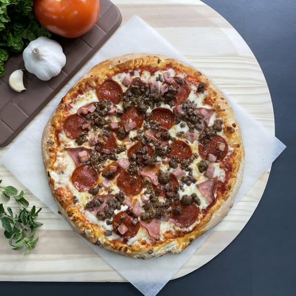 Big T's Pizza with pepperoni, ham, and ground beef, alongside fresh garlic, tomato, and greens.